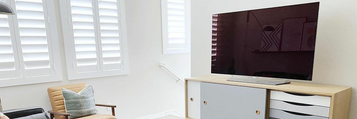 Modern living room with a large tv screen and white polywood shutters.